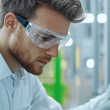 Man with beard, safety goggles and white shirt working in a biotech environment