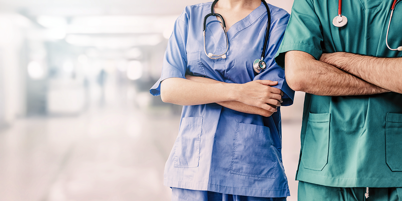The upper bodies of a woman and a man in the clothes of surgeons standing in a hospital corridor
