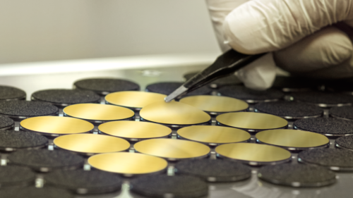 Close-up of several gold-coated membranes in the punching machine with tweezers detaching a membrane