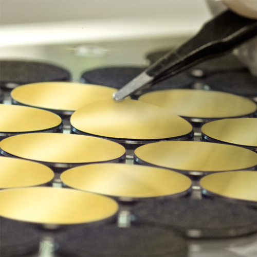Close-up of several gold-coated membranes in the punching machine with tweezers detaching a membrane