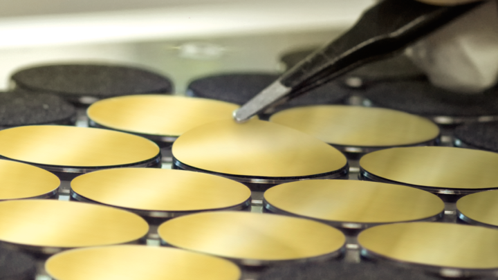Close-up of several gold-coated membranes in the punching machine with tweezers detaching a membrane