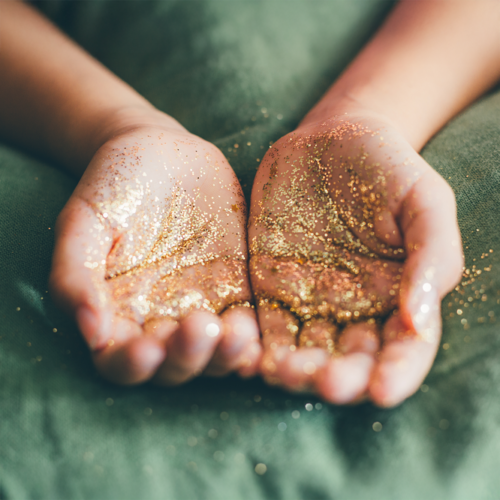 Two hands in a scooping pose with gold particles
