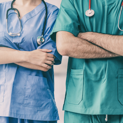 The upper bodies of a woman and a man in the clothes of surgeons standing in a hospital corridor